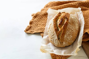 Çıtır ekşi ekmek, sıcak bir mutfak atmosferinde kırsal bir bez ve ahşap bir tahtanın eşlik ettiği etkin marş başlatıcısıyla dolu cam bir kavanozun yanında oturur..