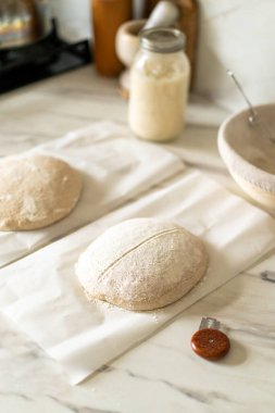 Taze hazırlanmış mayalı ekmek hamuru, aktif bir başlangıç kabı ve karıştırma kabının yanındaki parşömenin üzerinde duruyor..