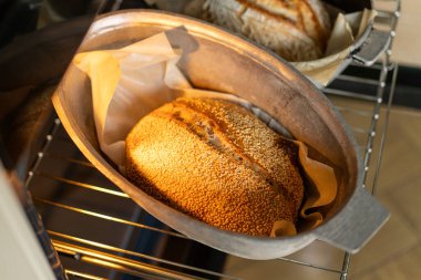 Fırının içindeki fırın kabuklarında duran iki altın-kahverengi somun ekmek, servis edilmeyi beklerken kabukları sıcaklıkla parlıyor. Davetkar koku havayı dolduruyor..