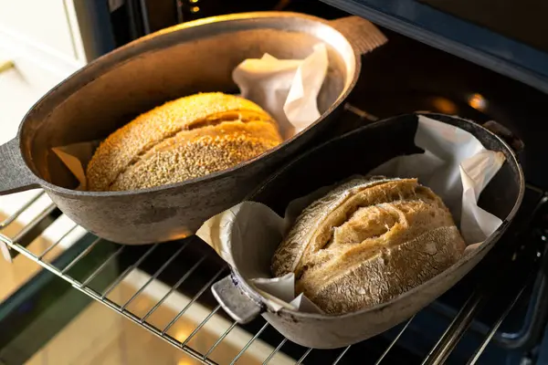 Fırının içindeki fırın kabuklarında duran iki altın-kahverengi somun ekmek, servis edilmeyi beklerken kabukları sıcaklıkla parlıyor. Davetkar koku havayı dolduruyor..