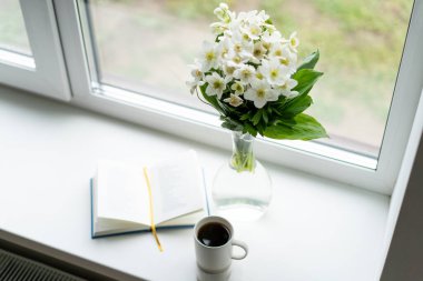 Pencere kenarında güzel bir yaz, sakin bir hayat. Bir buket beyaz çiçek Helleborus ve sıcak bir evin pencere eşiğinde bir kitap..