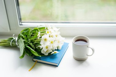 Pencere kenarında güzel bir yaz, sakin bir hayat. Bir buket beyaz çiçek Helleborus ve sıcak bir evin pencere eşiğinde bir kitap..