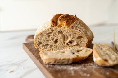 Çıtır ekşi ekmek, sıcak bir mutfak atmosferinde kırsal bir bez ve ahşap bir tahtanın eşlik ettiği etkin marş başlatıcısıyla dolu cam bir kavanozun yanında oturur..