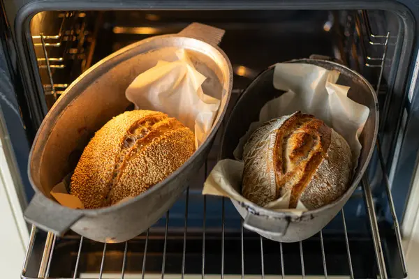 Fırının içindeki fırın kabuklarında duran iki altın-kahverengi somun ekmek, servis edilmeyi beklerken kabukları sıcaklıkla parlıyor. Davetkar koku havayı dolduruyor..