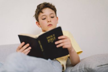 Bir çocuk kutsal kitabı okuyor ve dua ediyor ya da meditasyon yapıyor. Hıristiyanlık, din ve inanç kavramı.