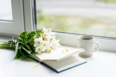 Pencere kenarında güzel bir yaz, sakin bir hayat. Bir buket beyaz çiçek Helleborus ve sıcak bir evin pencere eşiğinde bir kitap..