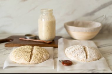 Taze hazırlanmış mayalı ekmek hamuru, aktif bir başlangıç kabı ve karıştırma kabının yanındaki parşömenin üzerinde duruyor..