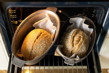 Fırının içindeki fırın kabuklarında duran iki altın-kahverengi somun ekmek, servis edilmeyi beklerken kabukları sıcaklıkla parlıyor. Davetkar koku havayı dolduruyor..