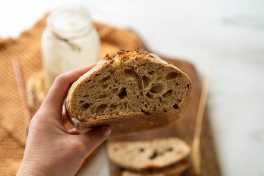 Çıtır ekşi ekmek, sıcak bir mutfak atmosferinde kırsal bir bez ve ahşap bir tahtanın eşlik ettiği etkin marş başlatıcısıyla dolu cam bir kavanozun yanında oturur..