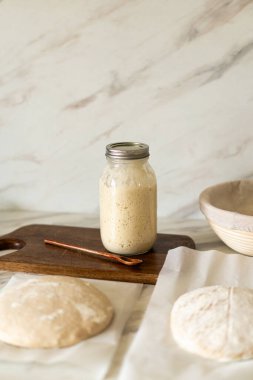 Taze hazırlanmış mayalı ekmek hamuru, aktif bir başlangıç kabı ve karıştırma kabının yanındaki parşömenin üzerinde duruyor..