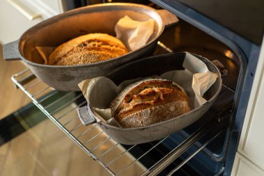 Fırının içindeki fırın kabuklarında duran iki altın-kahverengi somun ekmek, servis edilmeyi beklerken kabukları sıcaklıkla parlıyor. Davetkar koku havayı dolduruyor..