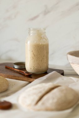 Taze hazırlanmış mayalı ekmek hamuru, aktif bir başlangıç kabı ve karıştırma kabının yanındaki parşömenin üzerinde duruyor..