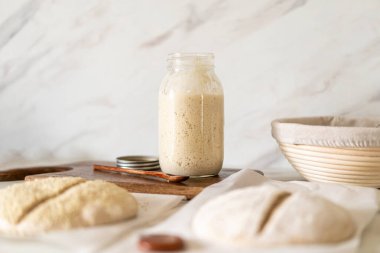 Taze hazırlanmış mayalı ekmek hamuru, aktif bir başlangıç kabı ve karıştırma kabının yanındaki parşömenin üzerinde duruyor..