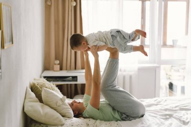 Evde çekilmiş bir erkek bebek portresi. Annesi yatakta dinleniyor ve hafta sonu birlikte yatakta oynuyor. Tembel bir sabah, sıcak ve samimi bir sahne. Anne çocuğunu kucağına alıp öpüyor. Anneler günü konsepti