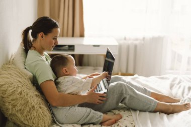 Evde dizüstü bilgisayar kullanan mutlu bir anne portresi. Birlikte, gülümseyen anne küçük oğluyla vakit geçirirken internette geziniyor..