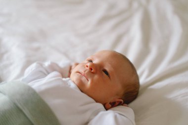 Yeni doğmuş bebek yumuşak bir battaniyenin altında uzanıyor, sakin bir sabah boyunca masumiyet ve merak dolu bir anı yakalıyor.