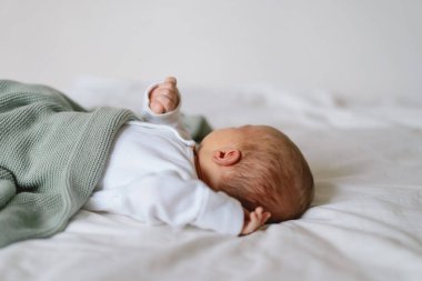 Yeni doğmuş bebek yumuşak bir battaniyenin altında uzanıyor, sakin bir sabah boyunca masumiyet ve merak dolu bir anı yakalıyor.