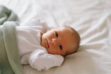 Yeni doğmuş bebek yumuşak bir battaniyenin altında uzanıyor, sakin bir sabah boyunca masumiyet ve merak dolu bir anı yakalıyor.