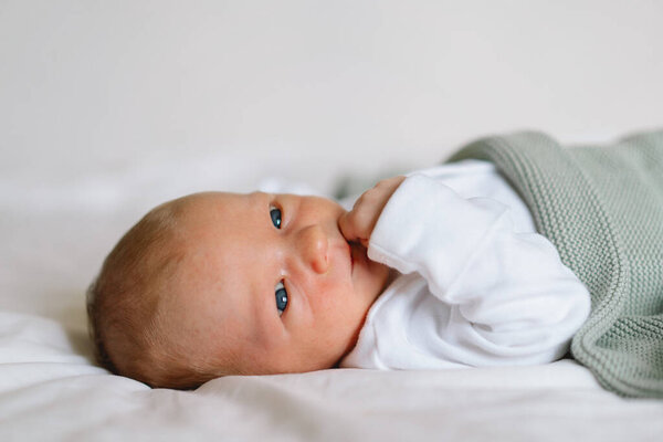 Новорожденный ребенок лежит на кровати под мягким одеялом, захватывая момент невинности и любопытства во время спокойного утра