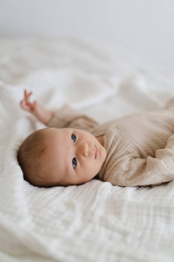 Cute baby lying on a soft white blanket with a calm expression while raising arms. Beautiful portrait of a child. Newborn baby lying on bed
