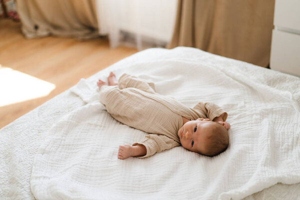 Cute baby lying on a soft white blanket with a calm expression while raising arms. Beautiful portrait of a child. Newborn baby lying on bed