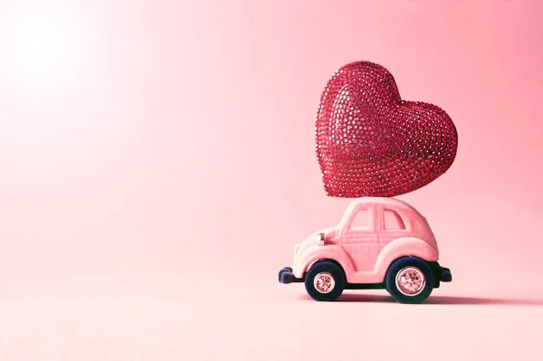 Retro toy car delivering craft heart for Valentine\'s day on pink background