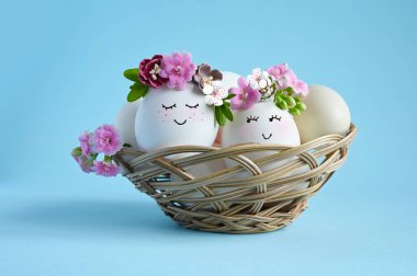 Mavi arka planda çiçek tacıyla çizilmiş gülen yüzlü doğal yumurtalar. Mutlu Paskalyalar.