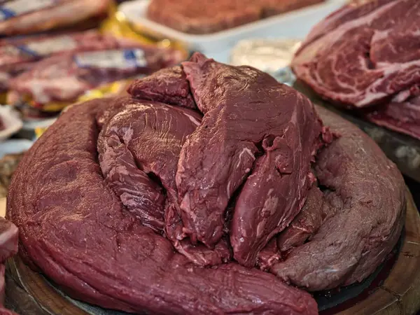 Restoranda seramik tabakta servis edilen çiğ bifteğin yakın plan görüntüsü. Bir şefin eli bıçakla taze eti pişirmeden önce keser. Geleneksel yemek hazırlıklarını doğal ışık ve otantik ortamlarla gösteren gerçekçi yemek fotoğrafçılığı.