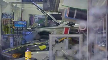 Balık ve baloncuklarla dolu bir akvaryumdan görülen araba tamir atölyesinin yaratıcı görüntüsü. Ön plandaki su ve yansımalar gerçeküstü ve sanatsal bir atmosfer yaratırken, mekanikler arka plandaki araç üzerinde çalışıyorlar..