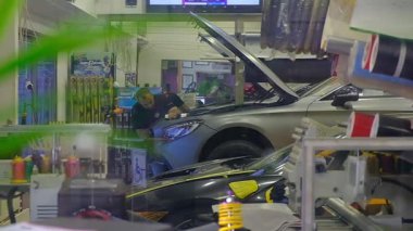 Balık ve baloncuklarla dolu bir akvaryumdan görülen araba tamir atölyesinin yaratıcı görüntüsü. Ön plandaki su ve yansımalar gerçeküstü ve sanatsal bir atmosfer yaratırken, mekanikler arka plandaki araç üzerinde çalışıyorlar..