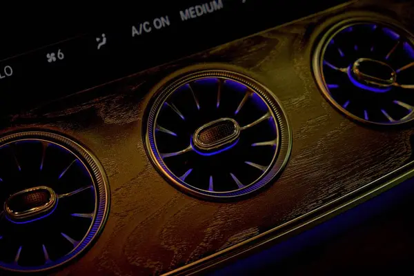 Aydınlatılmış dairesel menfezleri ve metalik dokusu olan araba klima paneline yakın çekim. Mavi ve turuncu renkli parlak ışıklı gelecekteki gösterge paneli tasarımı. Ticari kullanım için uygun. 