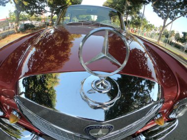 Caddeye güneş ışığı altında park edilmiş klasik kırmızı bir Mercedes Benz 280 SE Coupe. İkonik Alman lüks aracında krom bir ızgara, belirgin yuvarlak farlar ve 1960 'ların klasik tasarım detayları yer almaktadır..