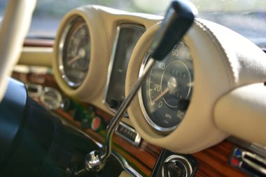 Caddeye güneş ışığı altında park edilmiş klasik kırmızı bir Mercedes Benz 280 SE Coupe. İkonik Alman lüks aracında krom bir ızgara, belirgin yuvarlak farlar ve 1960 'ların klasik tasarım detayları yer almaktadır..