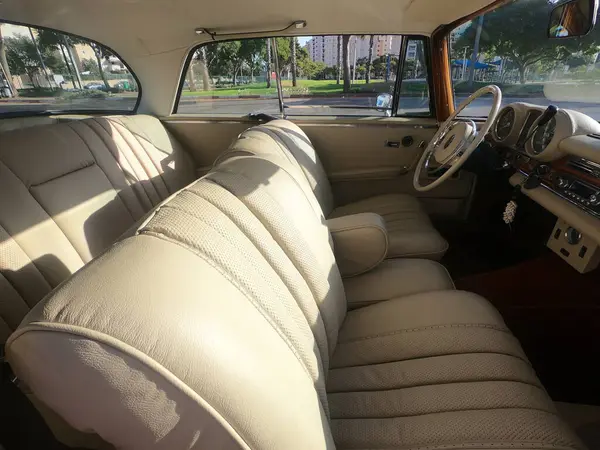 Caddeye güneş ışığı altında park edilmiş klasik kırmızı bir Mercedes Benz 280 SE Coupe. İkonik Alman lüks aracında krom bir ızgara, belirgin yuvarlak farlar ve 1960 'ların klasik tasarım detayları yer almaktadır..