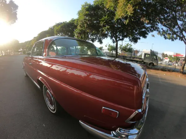 Caddeye güneş ışığı altında park edilmiş klasik kırmızı bir Mercedes Benz 280 SE Coupe. İkonik Alman lüks aracında krom bir ızgara, belirgin yuvarlak farlar ve 1960 'ların klasik tasarım detayları yer almaktadır..
