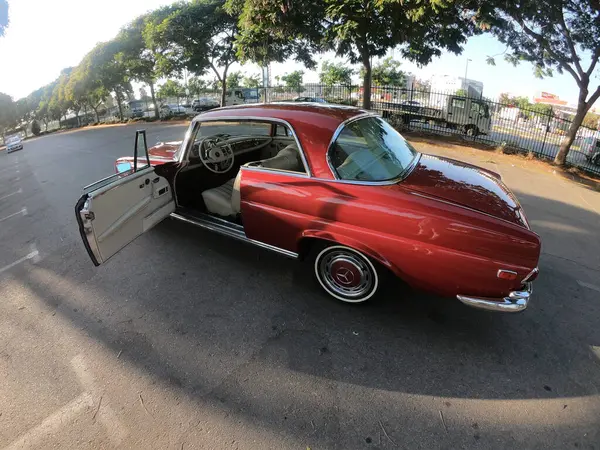 Caddeye güneş ışığı altında park edilmiş klasik kırmızı bir Mercedes Benz 280 SE Coupe. İkonik Alman lüks aracında krom bir ızgara, belirgin yuvarlak farlar ve 1960 'ların klasik tasarım detayları yer almaktadır..
