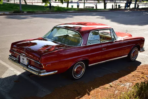 Caddeye güneş ışığı altında park edilmiş klasik kırmızı bir Mercedes Benz 280 SE Coupe. İkonik Alman lüks aracında krom bir ızgara, belirgin yuvarlak farlar ve 1960 'ların klasik tasarım detayları yer almaktadır..