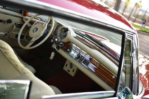 Caddeye güneş ışığı altında park edilmiş klasik kırmızı bir Mercedes Benz 280 SE Coupe. İkonik Alman lüks aracında krom bir ızgara, belirgin yuvarlak farlar ve 1960 'ların klasik tasarım detayları yer almaktadır..
