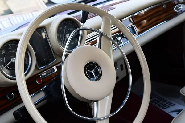 Caddeye güneş ışığı altında park edilmiş klasik kırmızı bir Mercedes Benz 280 SE Coupe. İkonik Alman lüks aracında krom bir ızgara, belirgin yuvarlak farlar ve 1960 'ların klasik tasarım detayları yer almaktadır..