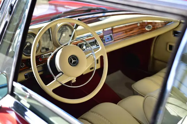 Caddeye güneş ışığı altında park edilmiş klasik kırmızı bir Mercedes Benz 280 SE Coupe. İkonik Alman lüks aracında krom bir ızgara, belirgin yuvarlak farlar ve 1960 'ların klasik tasarım detayları yer almaktadır..
