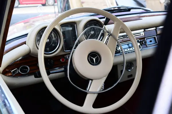 Caddeye güneş ışığı altında park edilmiş klasik kırmızı bir Mercedes Benz 280 SE Coupe. İkonik Alman lüks aracında krom bir ızgara, belirgin yuvarlak farlar ve 1960 'ların klasik tasarım detayları yer almaktadır..