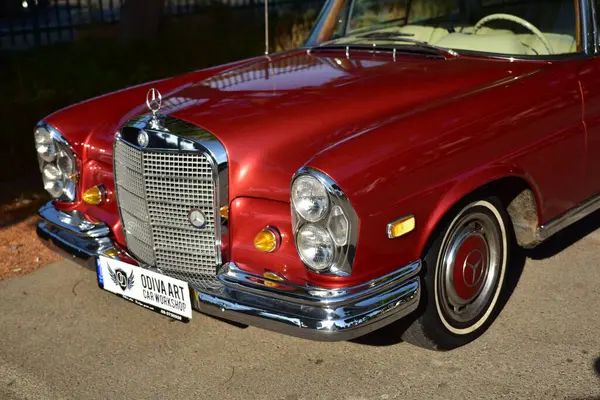 Caddeye güneş ışığı altında park edilmiş klasik kırmızı bir Mercedes Benz 280 SE Coupe. İkonik Alman lüks aracında krom bir ızgara, belirgin yuvarlak farlar ve 1960 'ların klasik tasarım detayları yer almaktadır..
