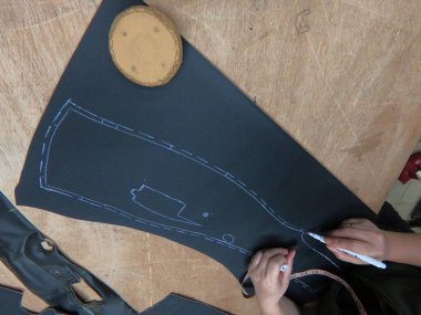 Bir araba servisi atölyesinde özel araba döşemesi için siyah deri ya da sentetik malzeme kesip hazırlamak. Elleri yakın plan işaretleme, makasla kesme, ve malzeme parçalarını şekillendirme.