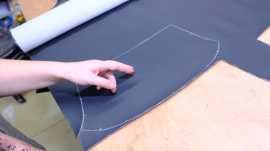 Bir araba servisi atölyesinde özel araba döşemesi için siyah deri ya da sentetik malzeme kesip hazırlamak. Elleri yakın plan işaretleme, makasla kesme, ve malzeme parçalarını şekillendirme.