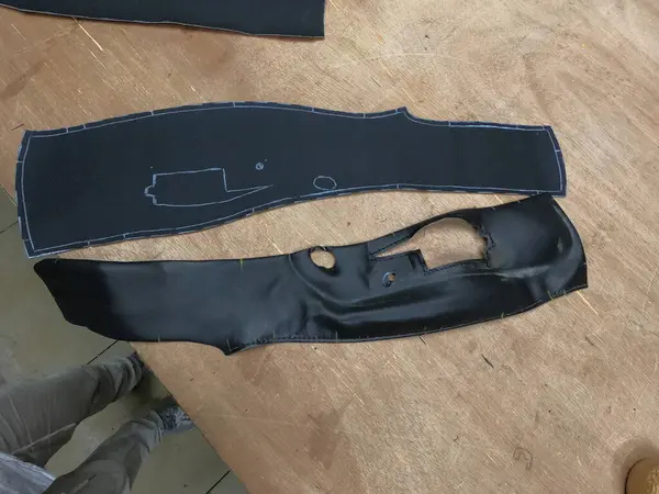 Bir araba servisi atölyesinde özel araba döşemesi için siyah deri ya da sentetik malzeme kesip hazırlamak. Elleri yakın plan işaretleme, makasla kesme, ve malzeme parçalarını şekillendirme.