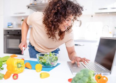 Cheerful black woman learning to cook at home watching online tutorial