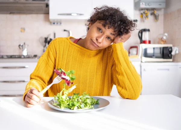 Sad black woman dieting and eating salad at home