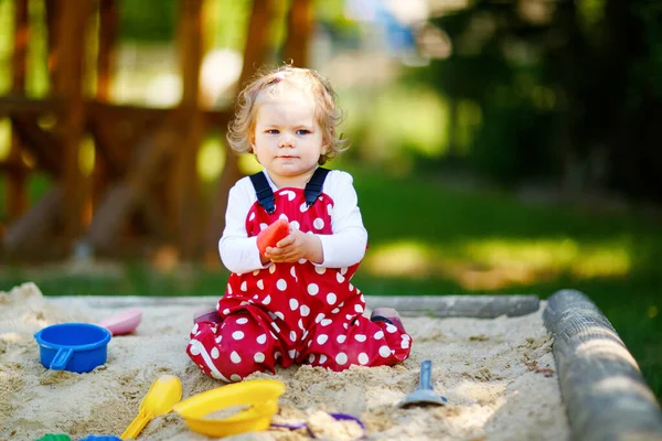 可爱的幼儿女孩在户外操场上玩沙子 美丽的宝宝穿着红胶裤 在阳光灿烂温暖的夏日里玩得很开心 带着五彩缤纷的沙玩具的孩子健康活泼的宝宝在户外玩游戏 — 图库照片