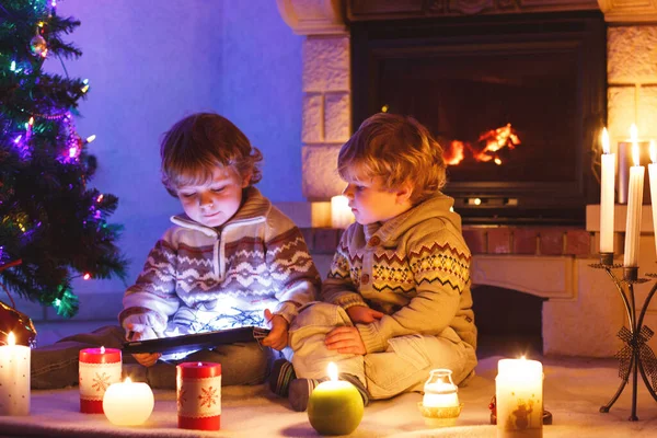 圣诞节的时候 两个小孩坐在壁炉边 快乐可爱可爱的幼儿男孩 金发碧眼的双胞胎玩新的平板礼物 庆祝圣诞节的家庭 — 图库照片