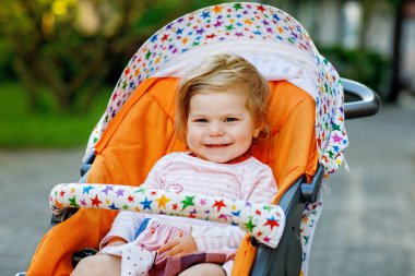 Bebek arabasında ya da bebek arabasında oturan ve yürüyüşe çıkan tatlı, gülümseyen bir kızın portresi. Mutlu şirin bebek dışarıda eğleniyor. Sağlıklı kız.
